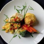 Chilean Sea Bass with a Pineapple Mango Chutney sits on a white plate with two sprigs of herbs on top of it.