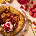 To the left side of the photo sits an Stone Fruit Galette, we see it from above, and it holds a scoop of vanilla ice cream on top.
