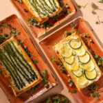 An above shot of three rectangular serving platters holding Herbed Goat Cheese Tart with Summer Vegetables