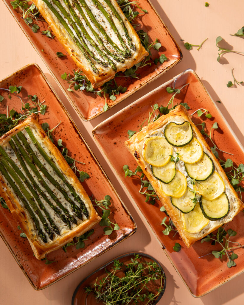 An above shot of three rectangular serving platters holding Herbed Goat Cheese Tart with Summer Vegetables