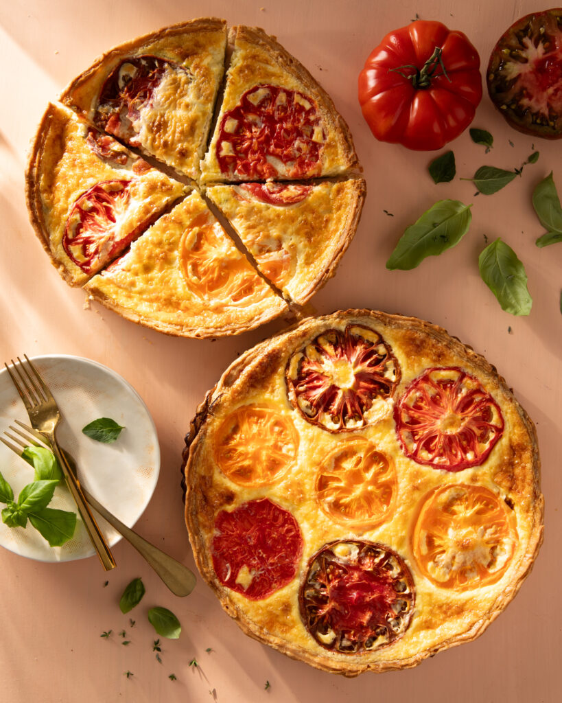 An above shot of two Heirloom Tomato and Cheddar Custard Tarts. One is cut into 5 pieces, the other is unsliced.