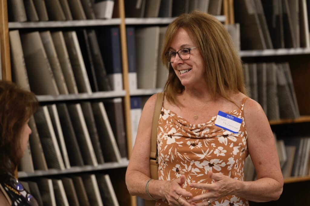 A woman in an orange floral dress stands in front of a tile shelf.