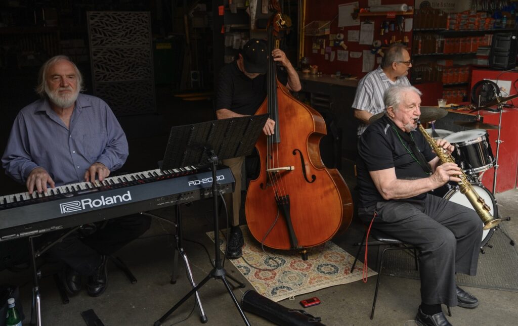 A quartet with clarinet, drums, keys, and bass plays in a garage.