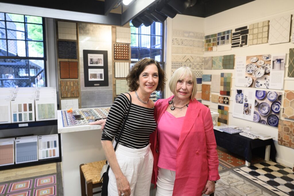 A woman in a black and white shirt and a woman in a pink shirt and blazer stand together in a tile show room.