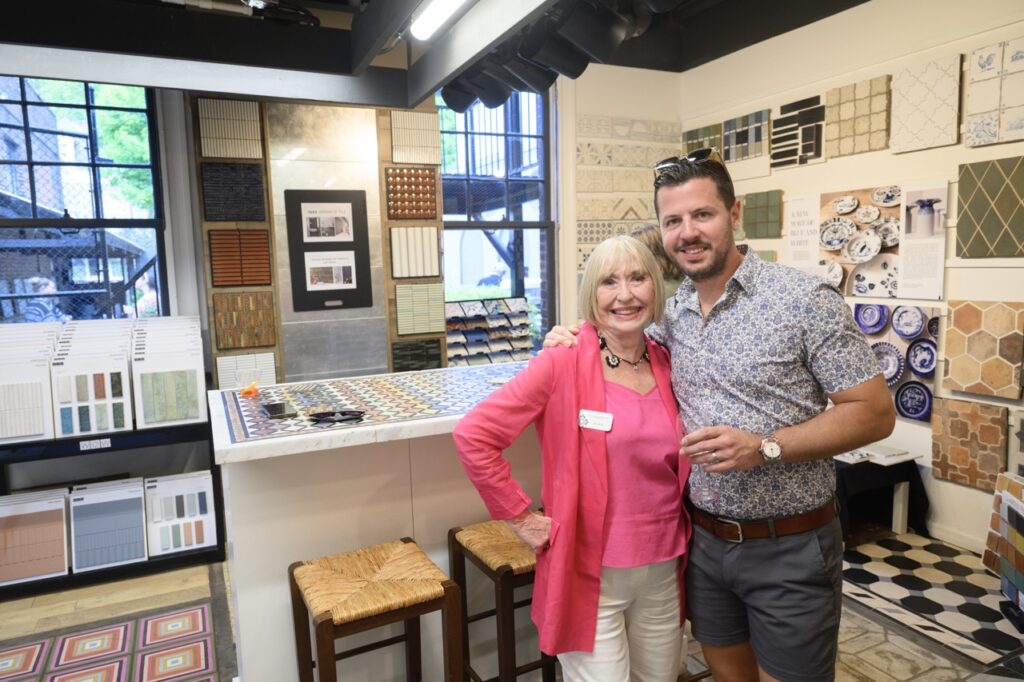A woman in a pink shirt and jacket and a man in a pattern blue shirt stand in a tile show space.