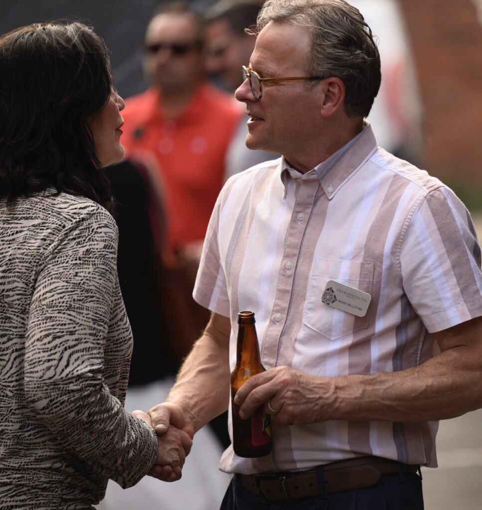 A man in a pink striped shirt shakes hands with a woman with dark hair.