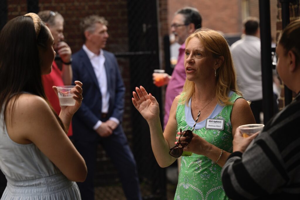 A woman in a green dress speaks to two other women.