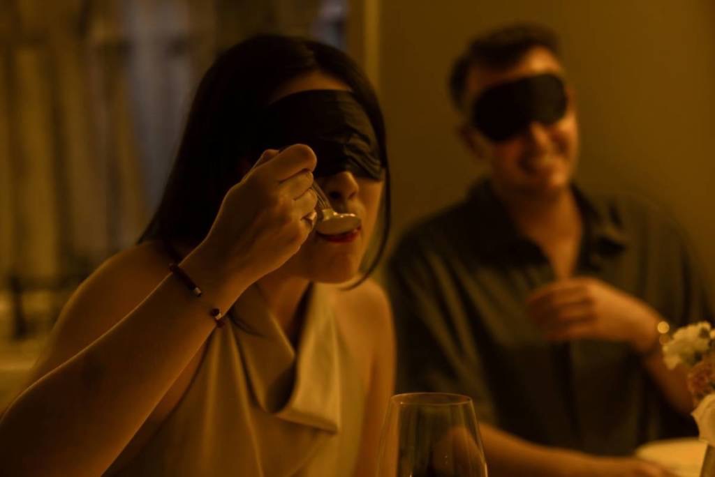 A woman takes a bite off a spoon with a blindfold on.