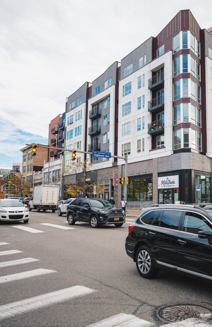 A busy street in East Liberty with cars going down it and a large building on the other side.