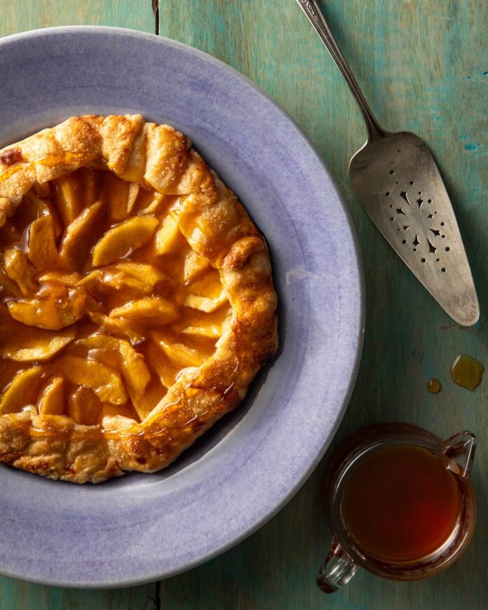 Easy Hot Honey Peach Galette A round Easy Hot Honey Peach Galette sits on a blue plate with a pie spatula sitting beside it.