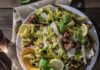 20 Minute Lazy Dinners A plate full of Easy Pesto Pasta with sausage, lemon slices, and asparagus all in a green sauce.