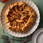 An easy hot honey apple galette sits in a round shape on a white plate with the edges of the galette folded in.