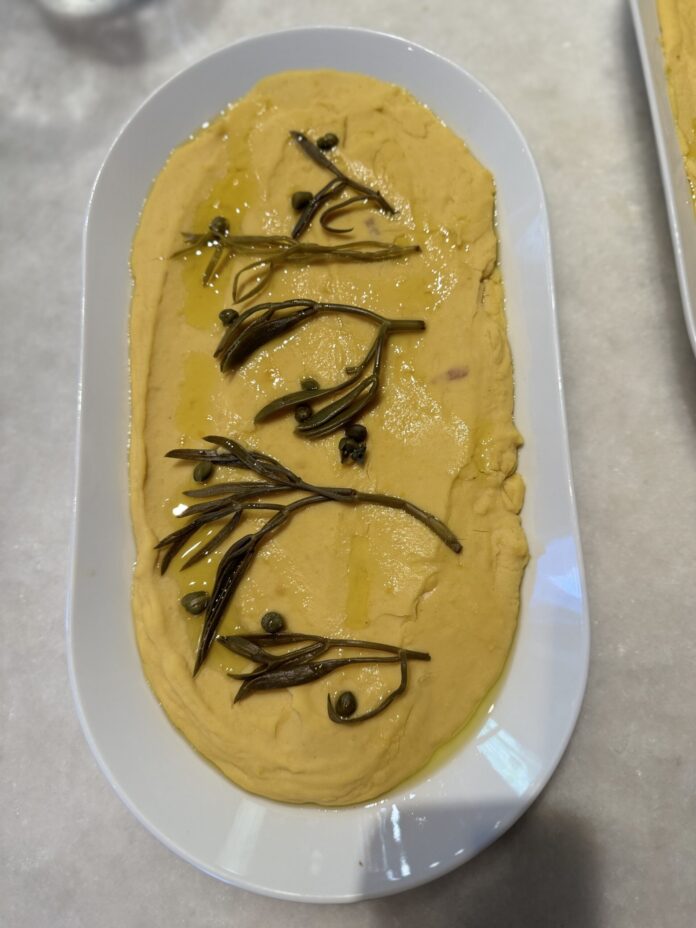 An aerial shot of a Fava Spread, yellow in color, on a white oval dish