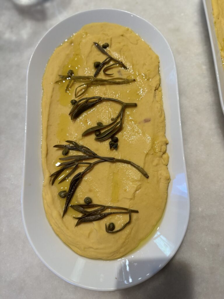 An aerial shot of a Fava Spread, yellow in color, on a white oval dish