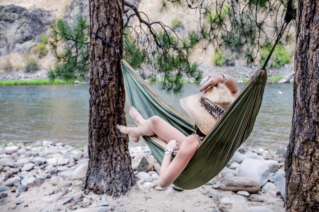 A woman lays in a green hammock on the shore.