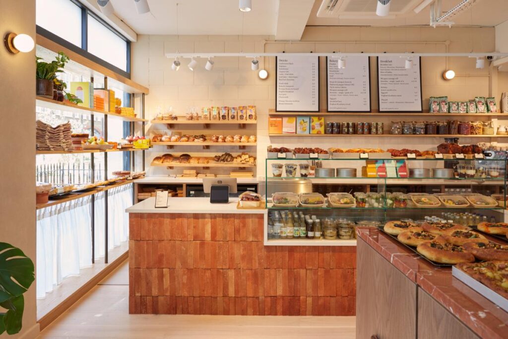 A wide shot of the Honey & Co. bakery and deli, showing shelves stocked with various food items and a counter with pastries and prepared foods.