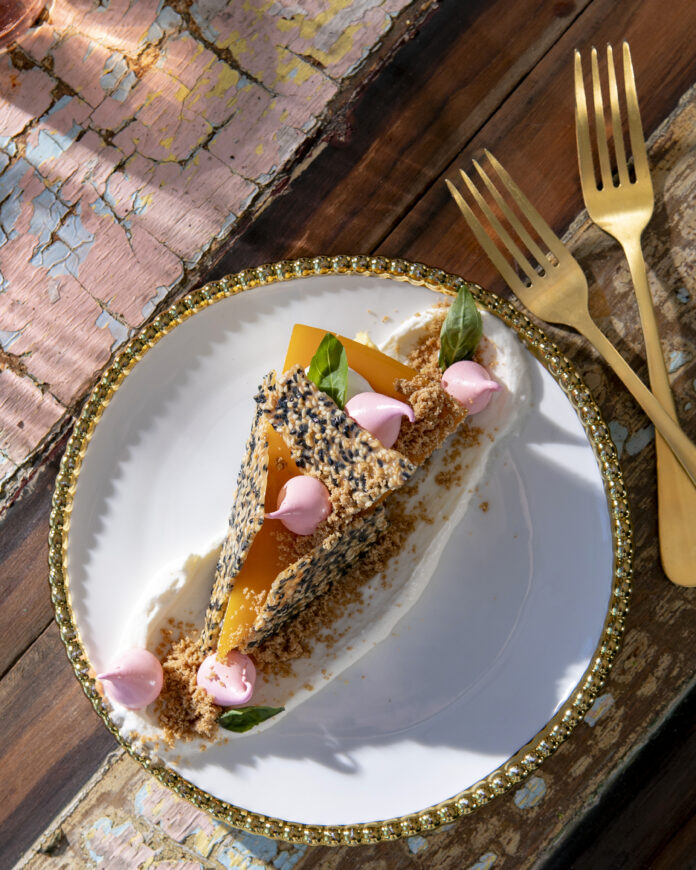 An above shot of a slice of Gluten Free Cheescake from Lilith, an Allergy-Sensitive Restaurant in Pittsburgh. The cheesecake is orange in color with a white, black, and brown seed-looking crumble on top.