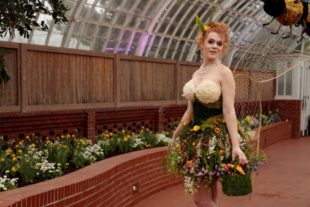 A woman in a flower dress stands in a garden.