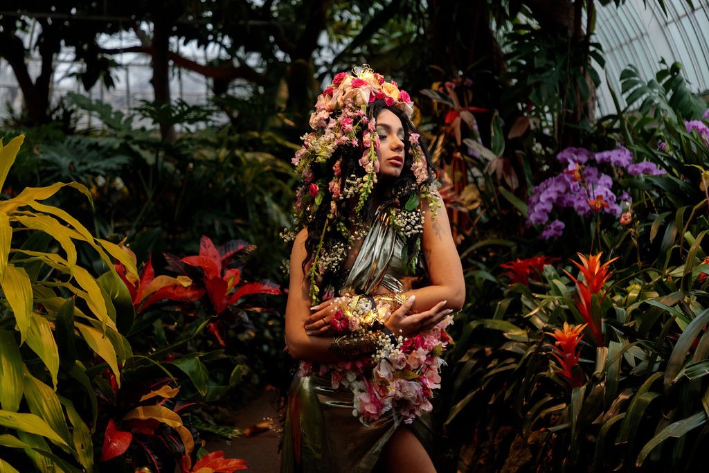 A woman covered in flowers stands in the florals.