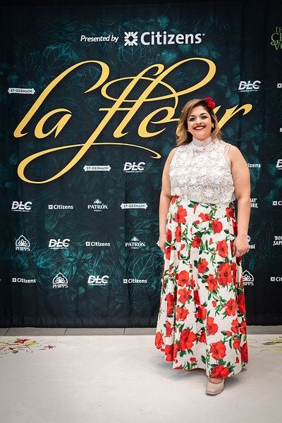 A woman in a white and floral dress stands in front of the le fleur sign.