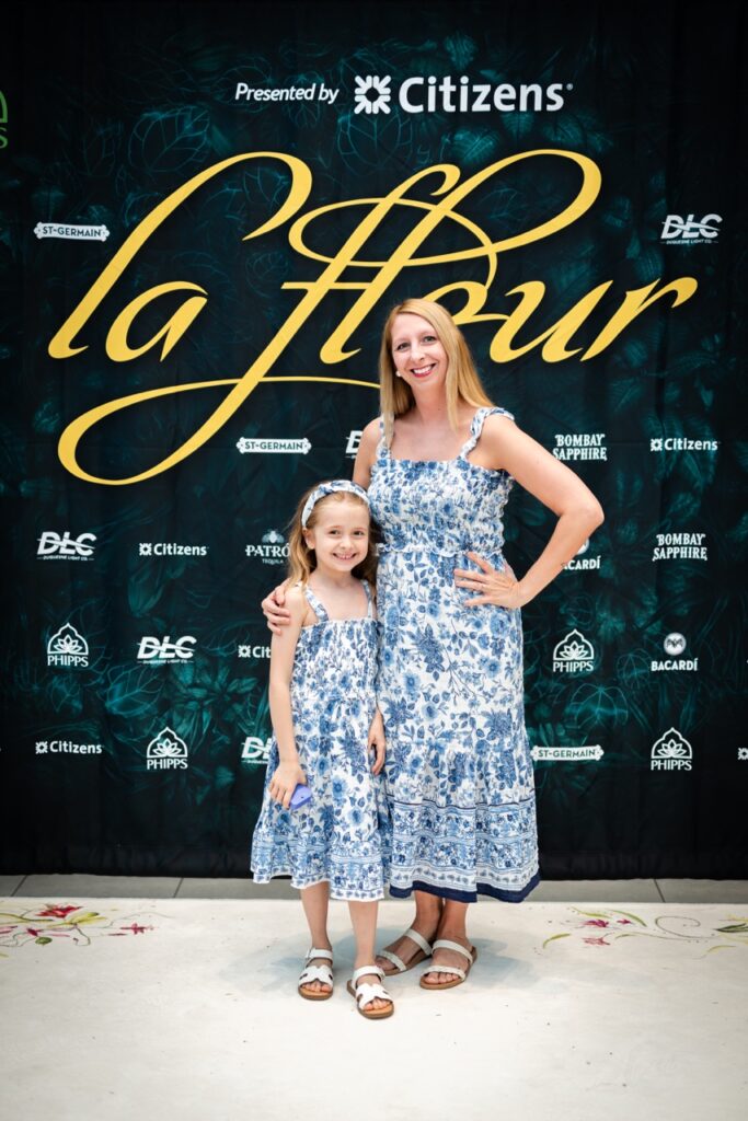 A woman in a blue and white dress stands beside her daughter in the same dress.