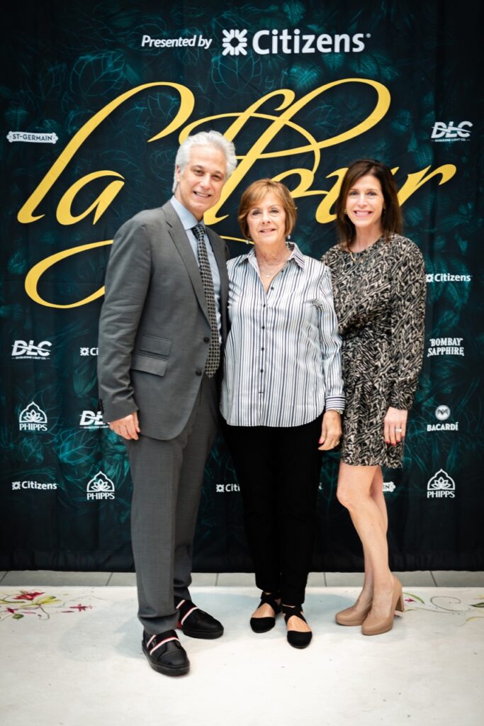 Two women and a man stand together in front of the La Fleur sign.