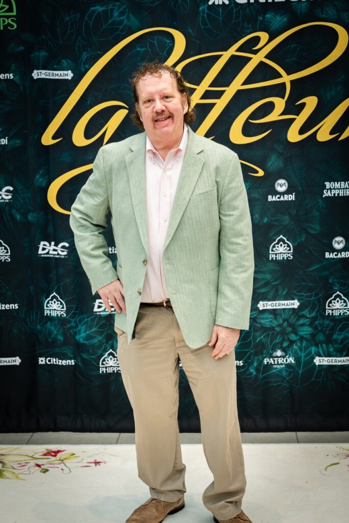 A man in a mint jacket poses in front of the La Fleur sign.