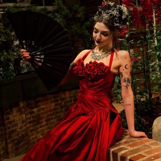A woman in a red dress sits on a brick wall.