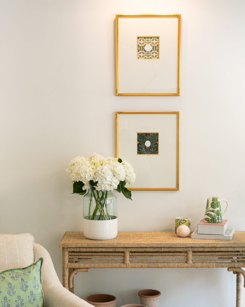 A small brown table holds a vase and sits below two framed photos.
