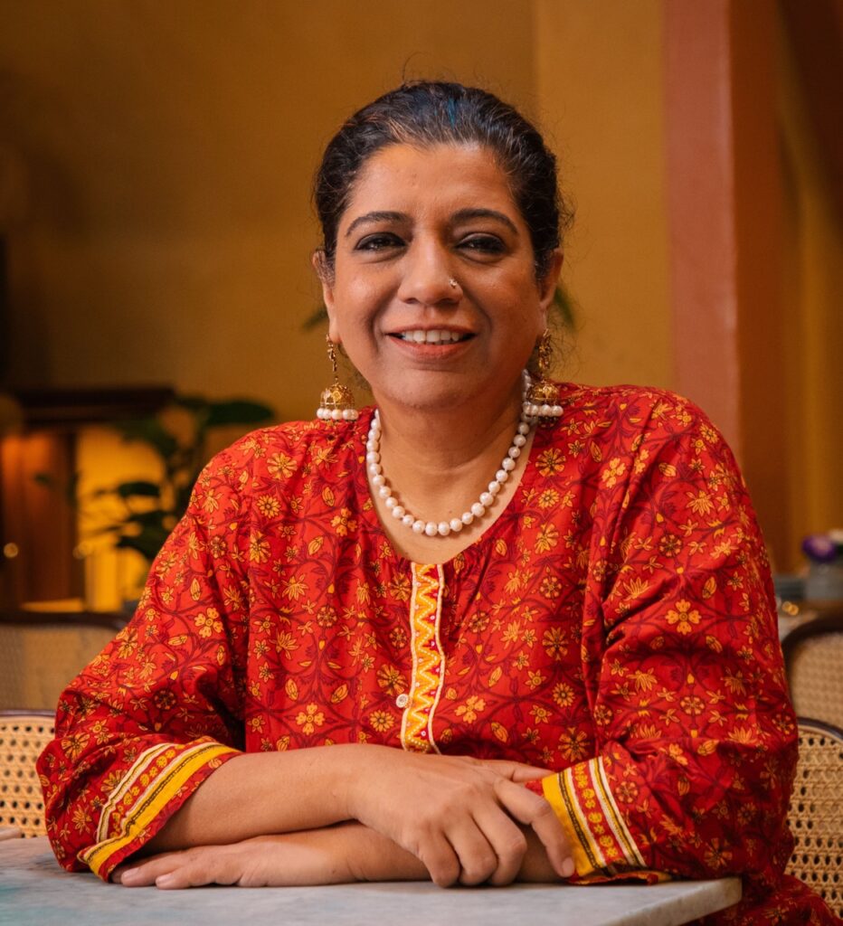 The woman chef at Darjeeling Express in London leans on a table with a red dress and dark hair.
