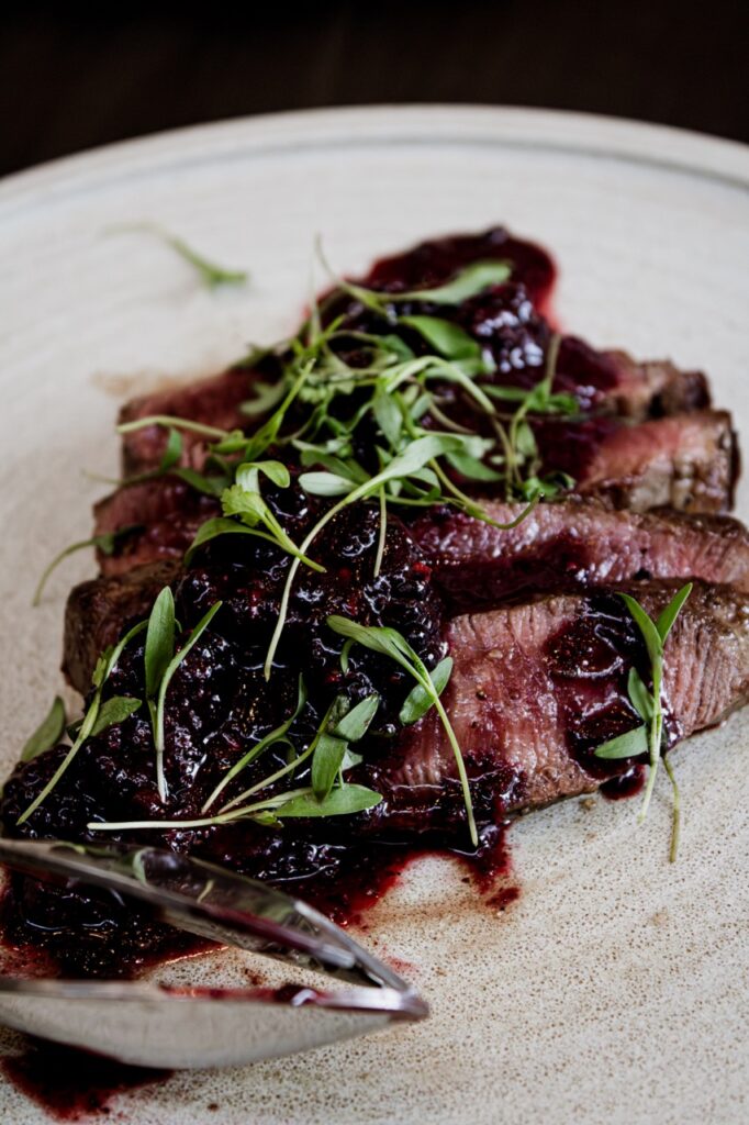 Slices of wagyu beef with a blackberry chimicurri and microgreens.