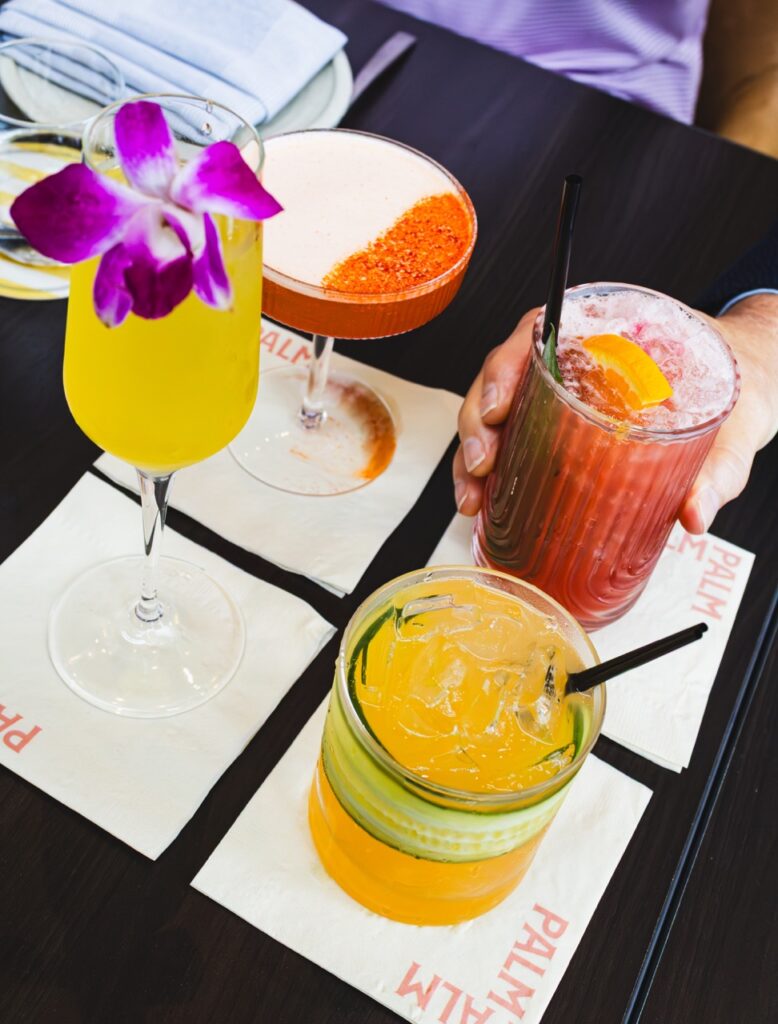 Four cocktails in yellow and red colors sit on individual square white cocktail napkins.
