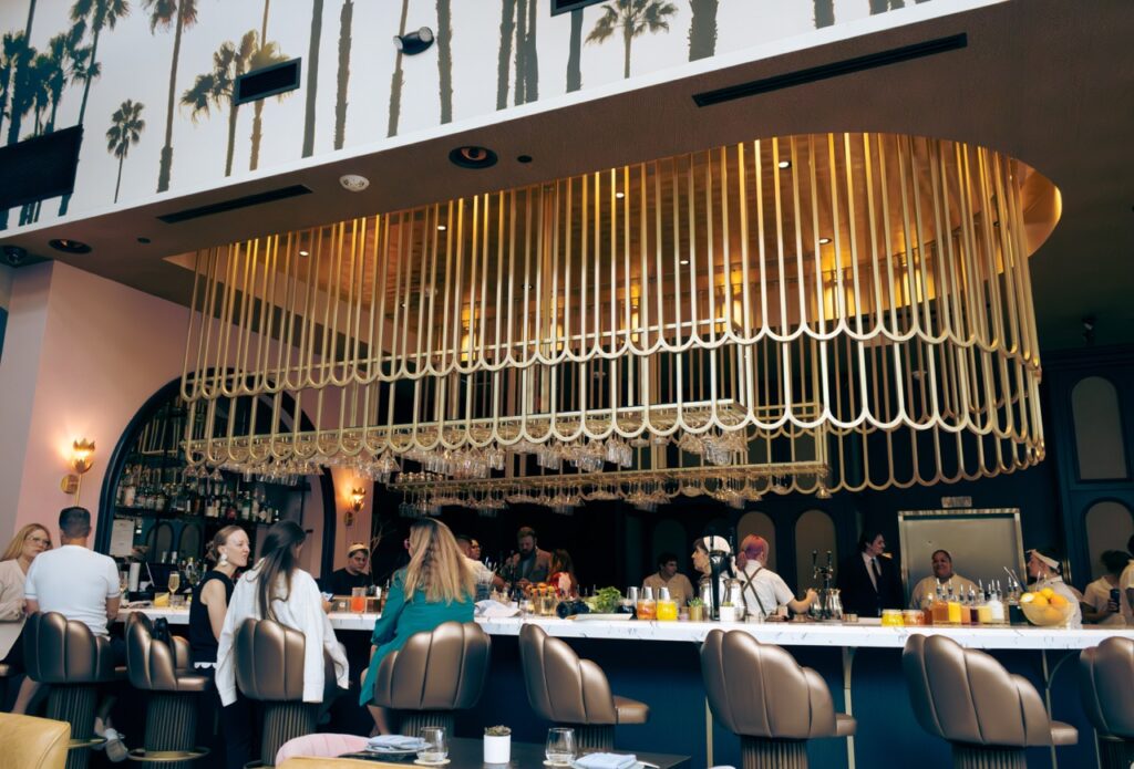 A long bar with people sitting in chairs with a mural of palm trees above it.