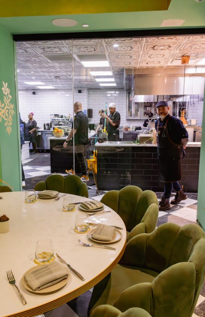 A private dining room with a round white table, green chairs, and a view into the kitche.