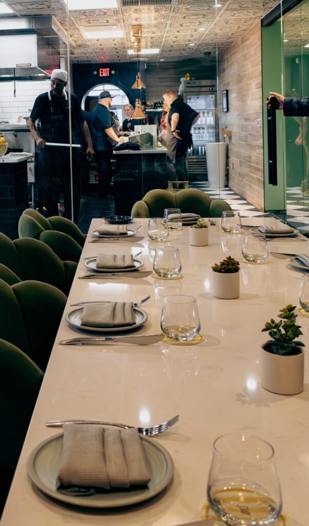 Palm Palm private dining room with a long white table, green chairs, and a view into the kitchen.