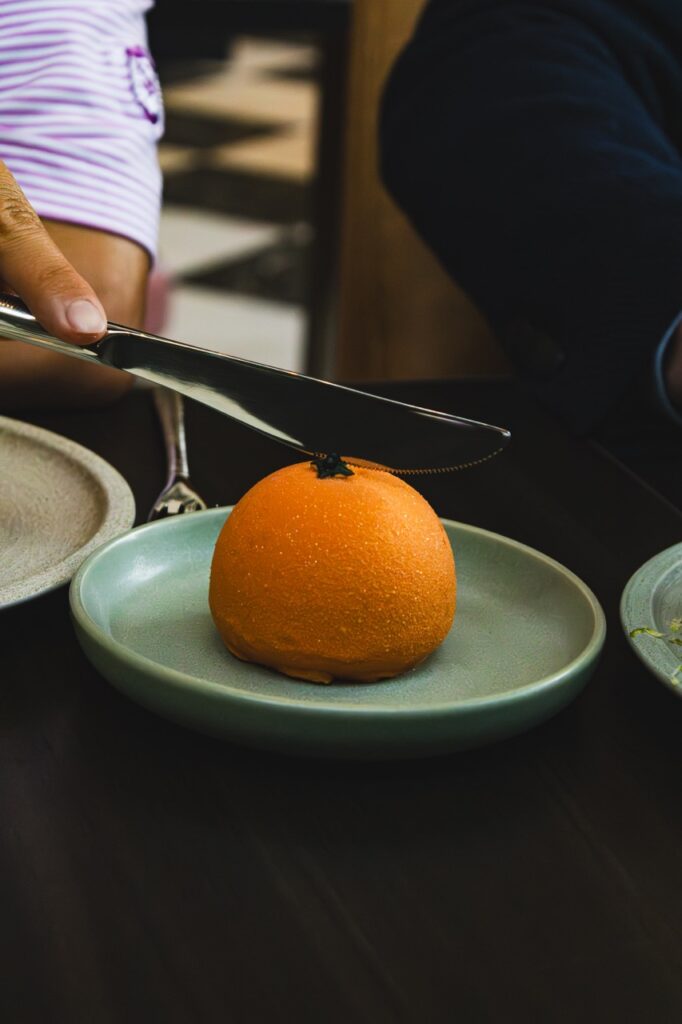 An orange fruit looking dessert with a person holding a knife over top of it.