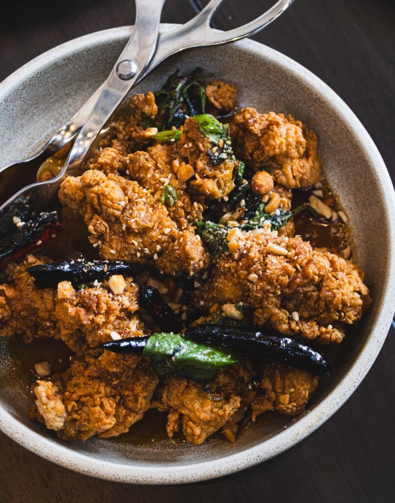 Chunks of Korean fried chicken sit with peppers in a white bowl.