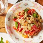 Della Terra's Panzanella Salad sits in a white and pink pattern bowl on a picnic like table below a fork.