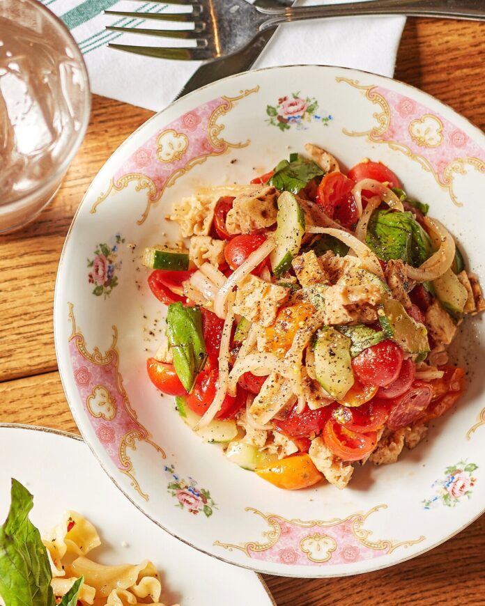 Della Terra's Panzanella Salad sits in a white and pink pattern bowl on a picnic like table below a fork.