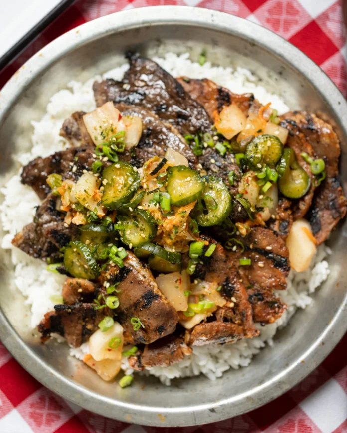An above shot of a metal bowl filled with a Korean BBQ combo featuring bulgogi, dwaejibulgogi, and kalbi.