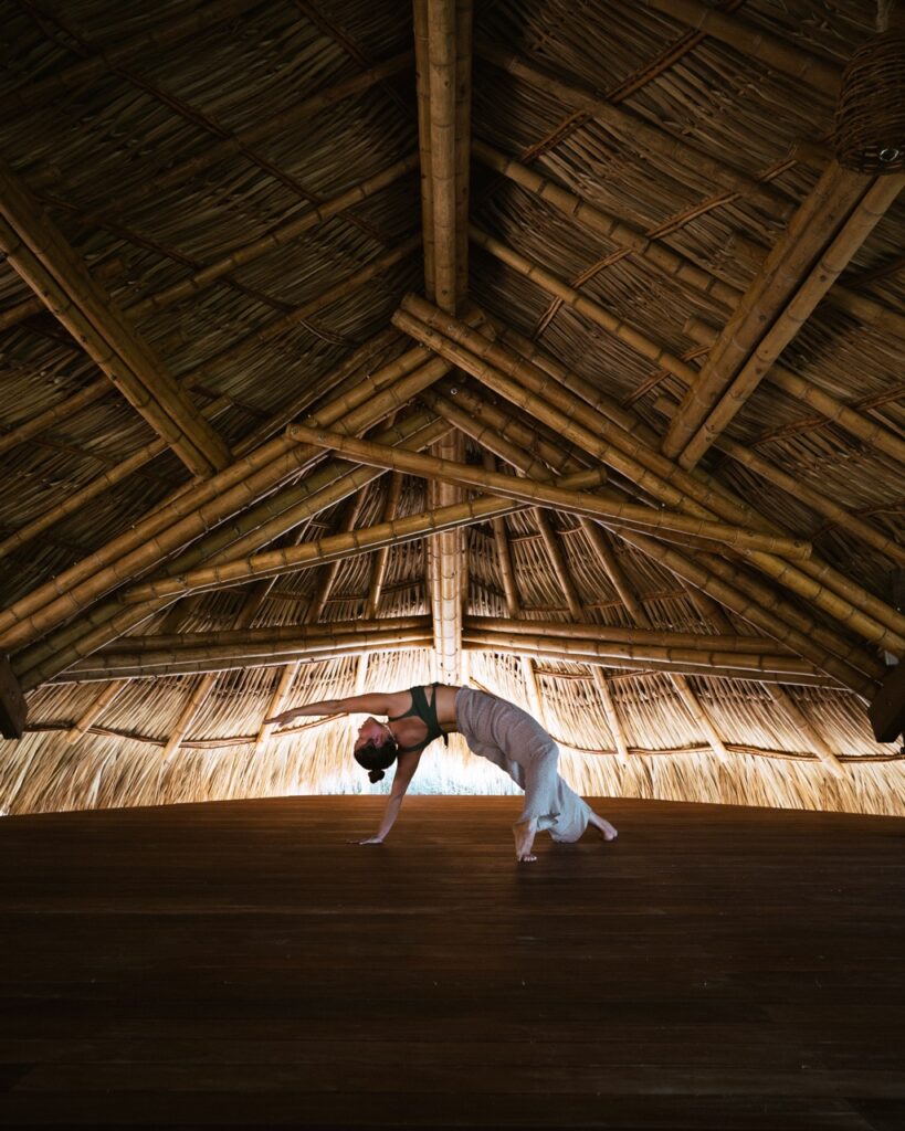 A woman bends back while practicing yoga in a bamboo hut.