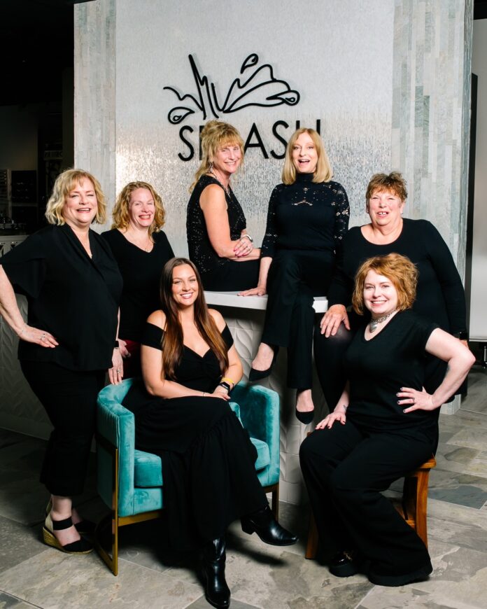 A group of women in black surround the splash logo and a blue chair.