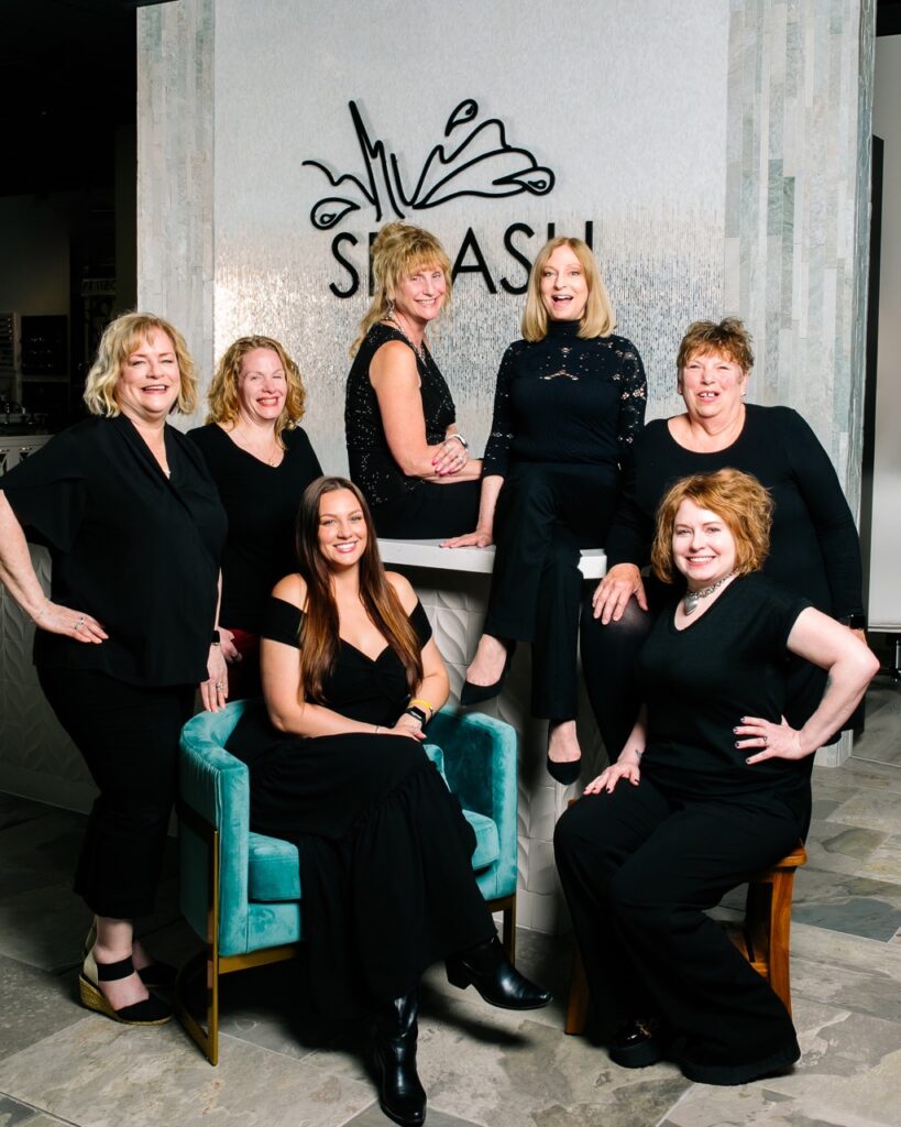 A group of women in black surround the splash logo and a blue chair.