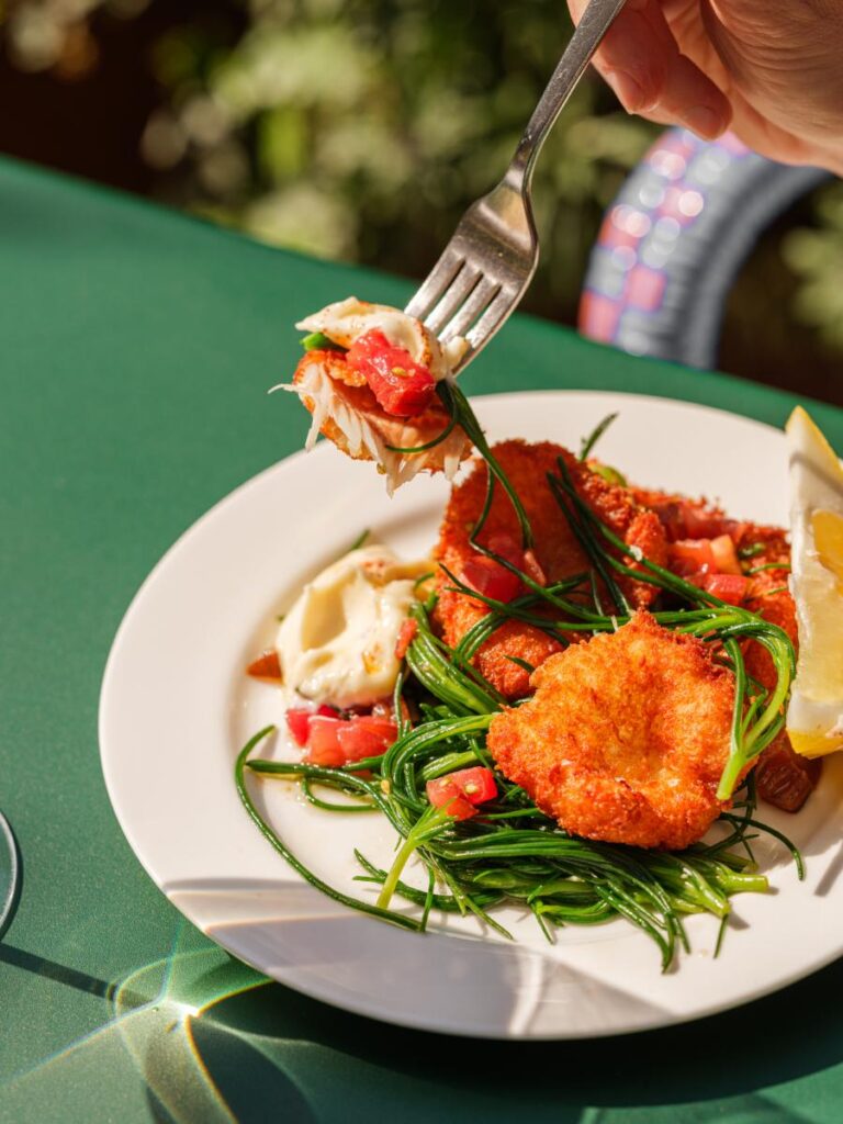 A vibrant dish with several fried, golden-brown pieces of food, possibly feta or fish cakes, garnished with green herbs and diced red tomatoes