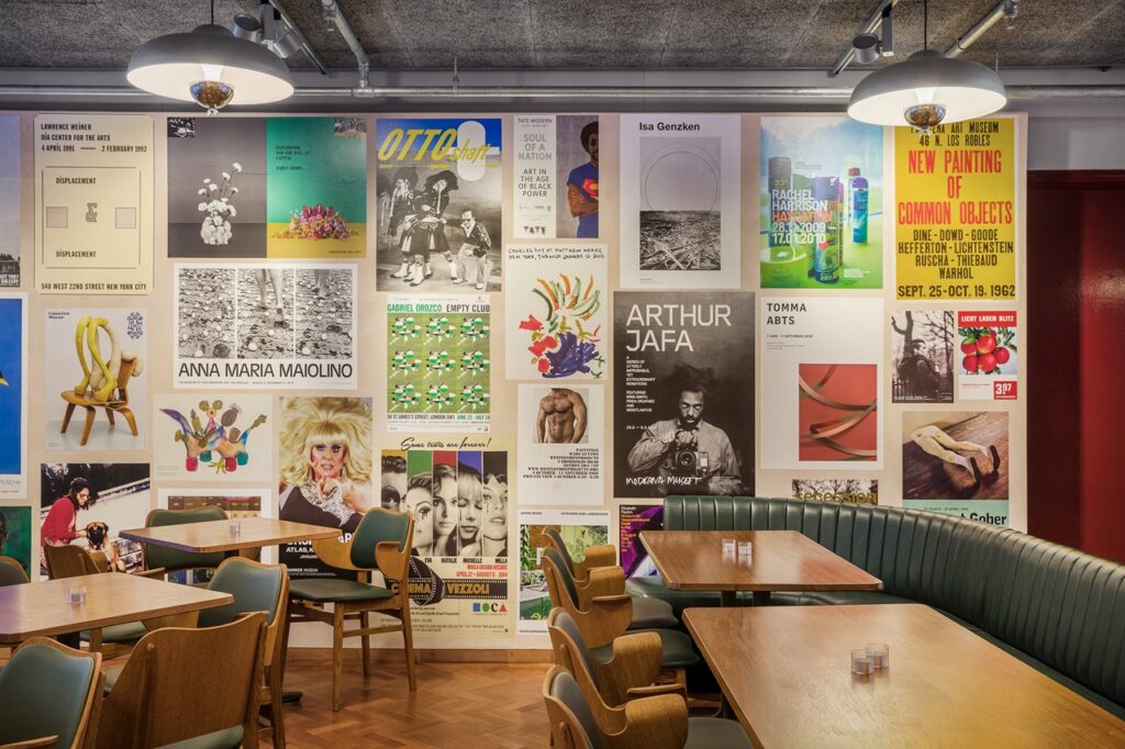 Posters adorn the wall of Toklas restaurant in London with wood tables throughout.
