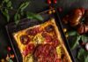 Easy Puff Pastry Tomato Pie A rectangular heirloom tomato pie with a flaky puff pastry crust, topped with colorful sliced tomatoes and fresh thyme, on a dark baking sheet surrounded by various whole and halved heirloom tomatoes and greenery.