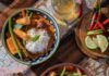 20 Minute Coconut Red Curry Two bowls of 20 minute coconut red curry sit on a table beside silverware, red chiles, lime slices, and a cup of beer.