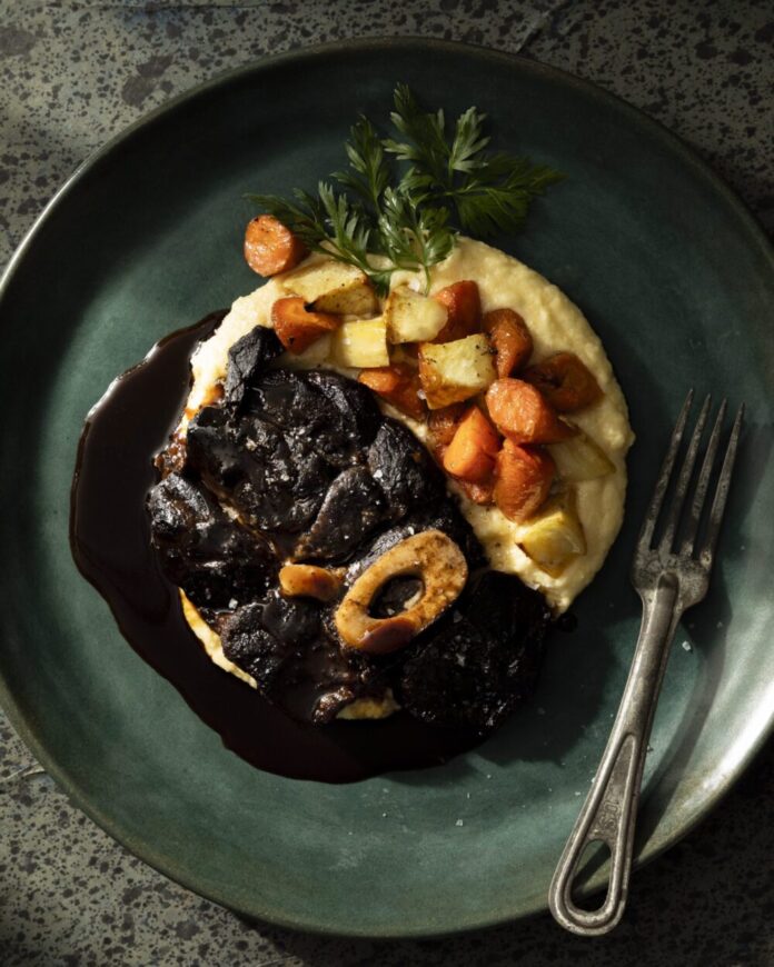 An above shot of a green plate with high edges, holding Beef Shank with Confit Garlic and Polenta