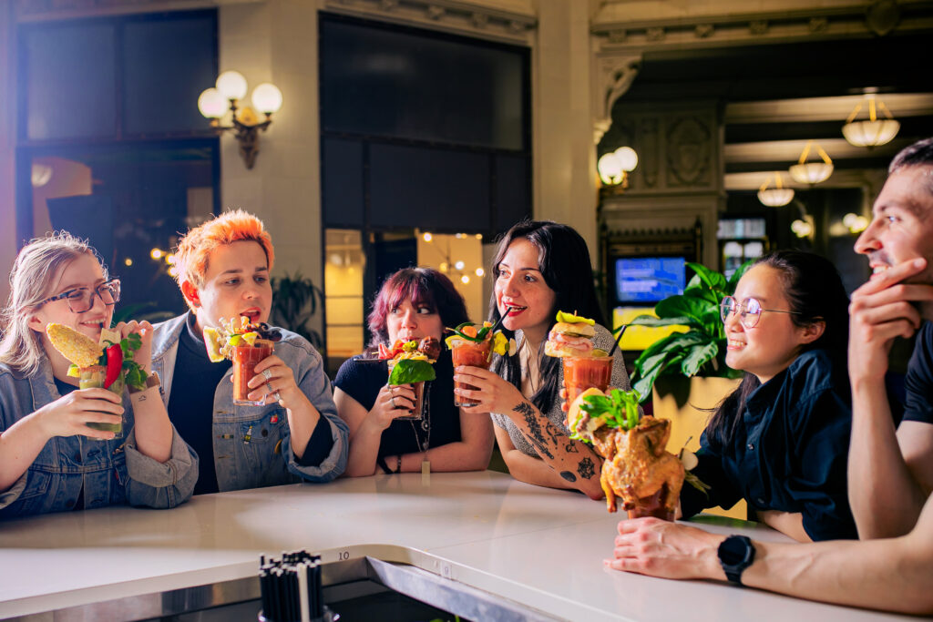 Six people sitting around a bar drinking loaded bloody Marys.