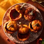 A platter holds six baked baby pumpkins, some with their tops removed and filled with a sauce.